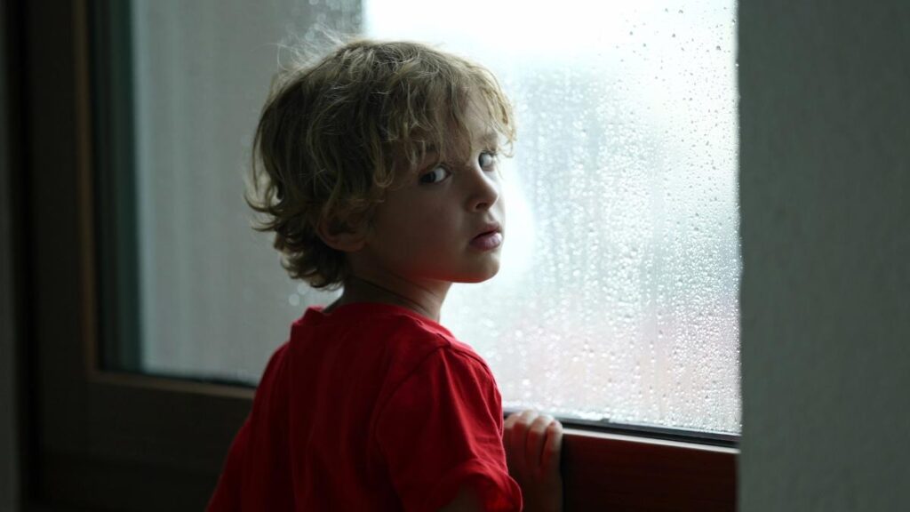 nervous little boy looking out window during storm