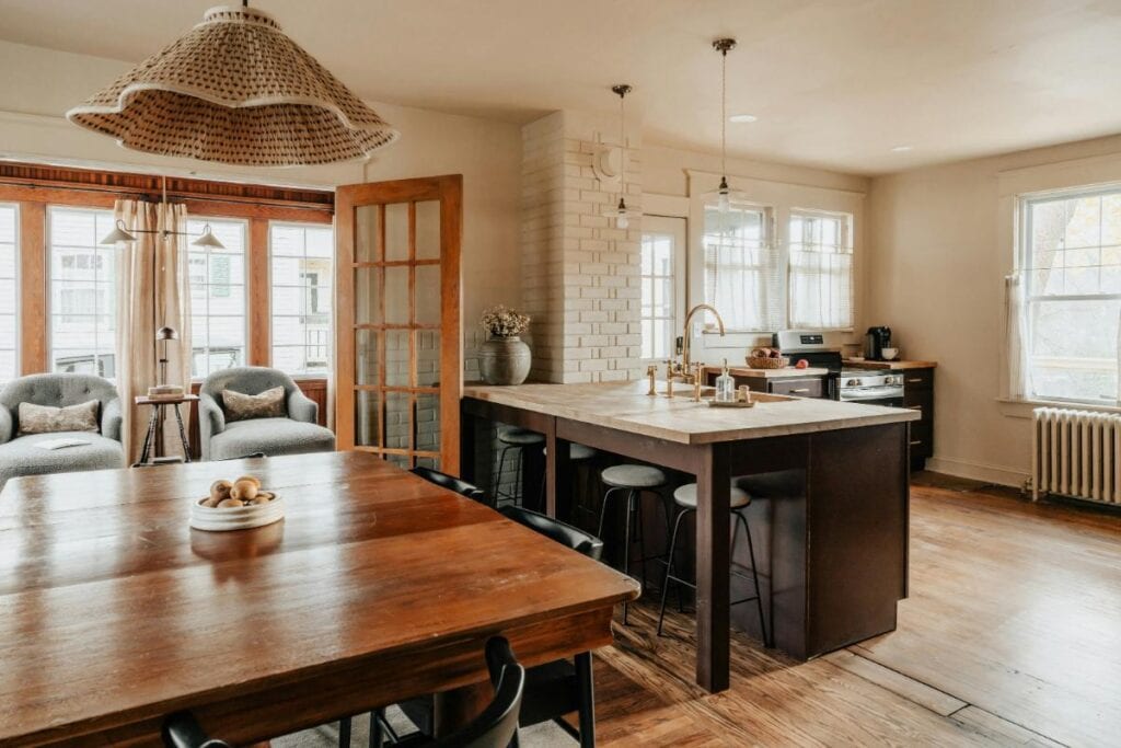 Warm open-plan kitchen and dining room with wood floors, large island, and layered lighting.